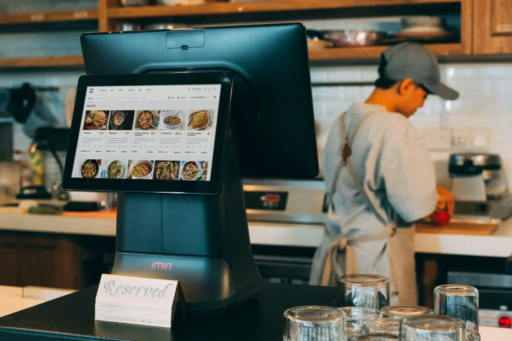 Sistema de pedidos com ecrã tátil ao balcão de um restaurante, com a cozinha ao fundo
